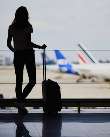 Eine Reisende steht mit Koffer am Fenster des Flughafens