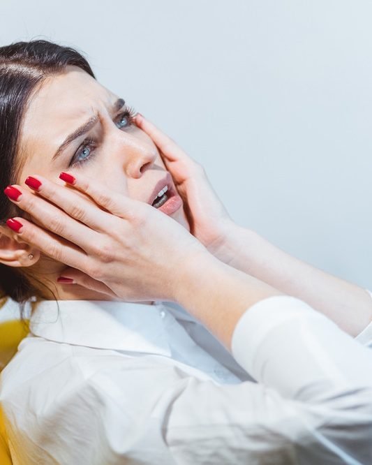 Eine Patientin hält sich im Behandlungsstuhl ängstlich die Wangen